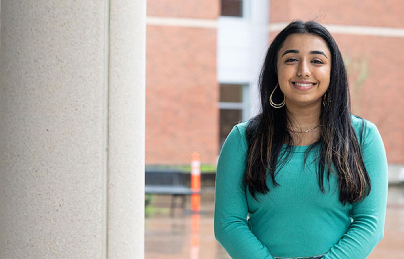 A person stands outside near a building column and smiles toward the camera.