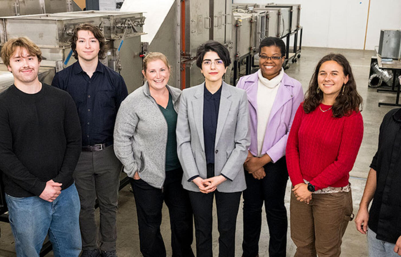 Seven people stand in a lab next to cylindrical equipment and look up toward the camera.