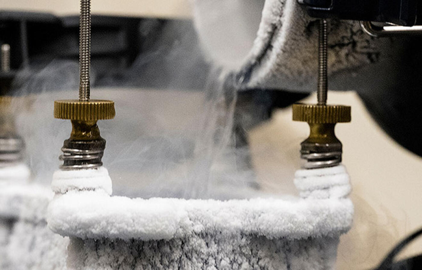 Liquid nitrogen is poured into a metal cooling pot mounted on computer hardware, with frost and vapor forming around the pot.
