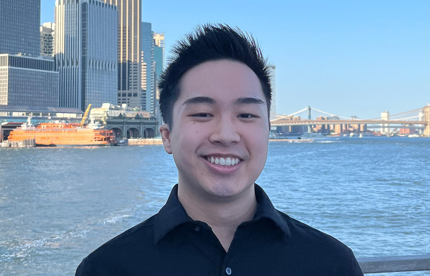 Chris Ho stands on a boat with the New York City skyline behind him.
