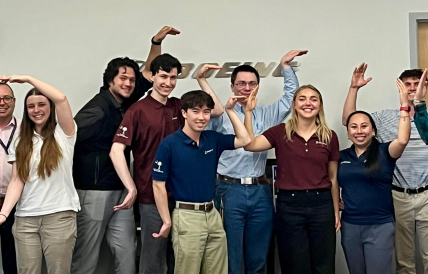 MECOP students in a conference room with the Boeing logo on the wall behind them and form the letters OSU with their arms.