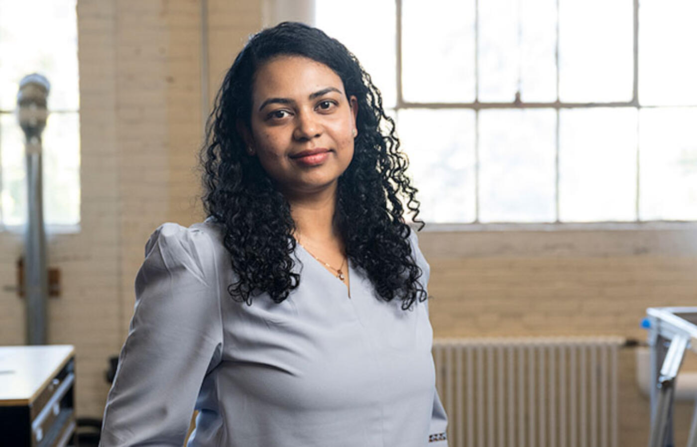 Sandhya Saisubramanian stands in a lab with windows behind her and workbenches and hardware in the background. 