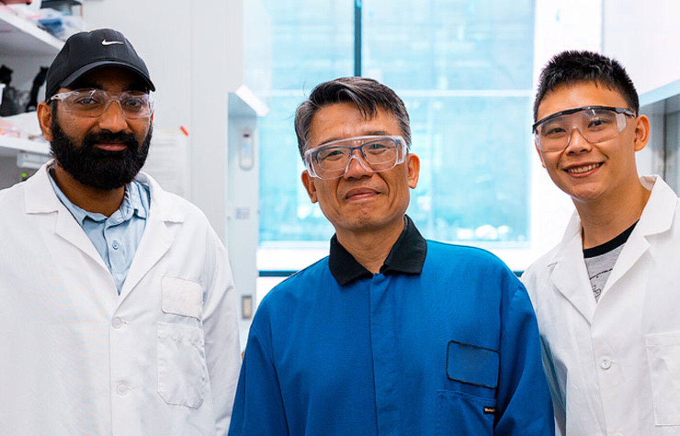 Venkata Vinay Doddapaneni, Chih-hung Chang, and Alvin Chang stand in a lab in Johnson Hall wearing lab coats and protective eyeglasses.