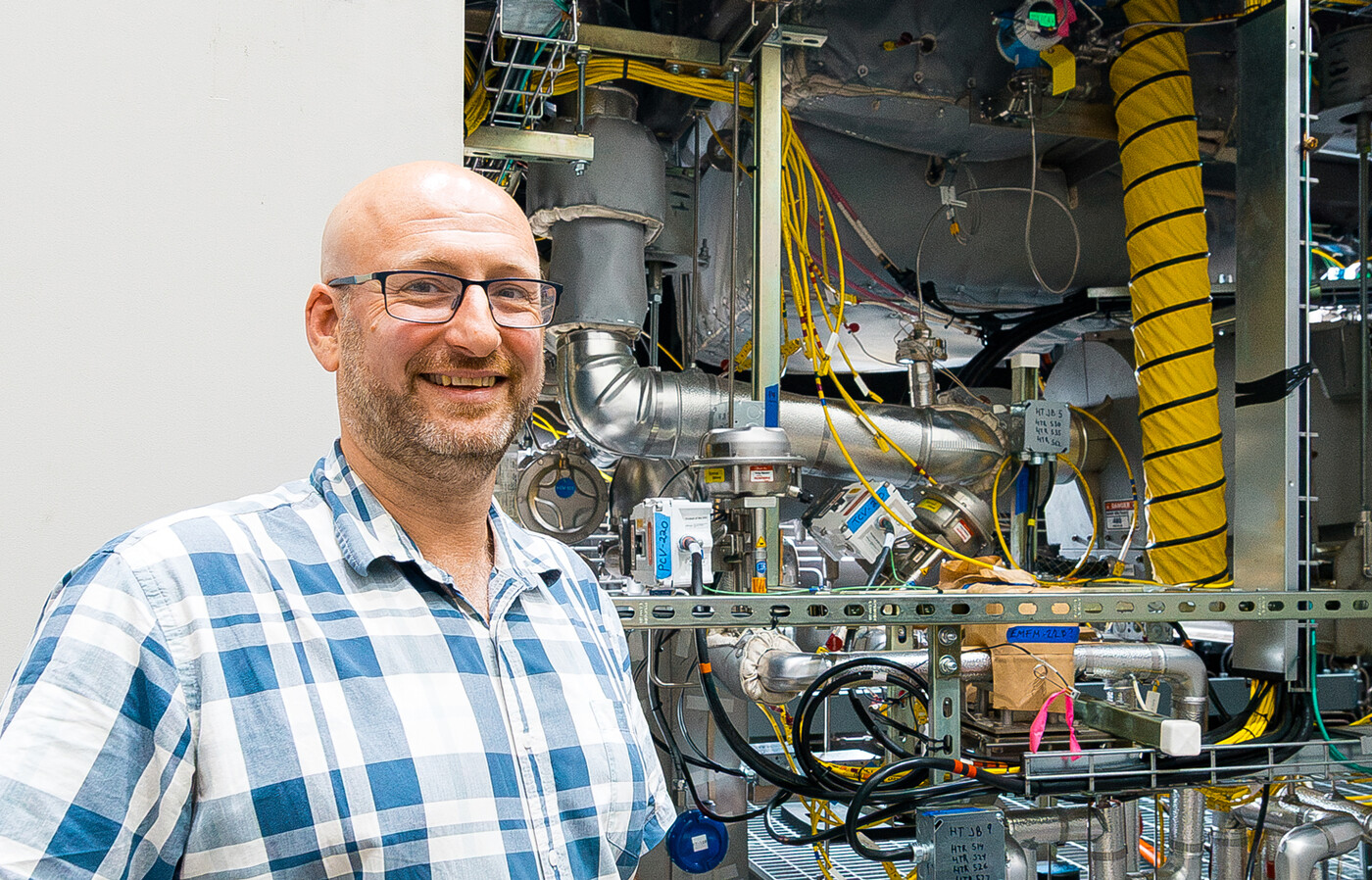 Guillaume Mignot stands outside beside a large instrument filled with pipes, cables, valves, and metal components.