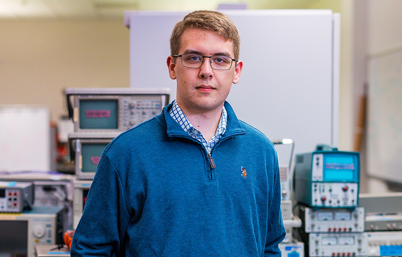 John Fletcher stands inside of a laboratory with testing equipment, workstations, and whiteboards in the background.