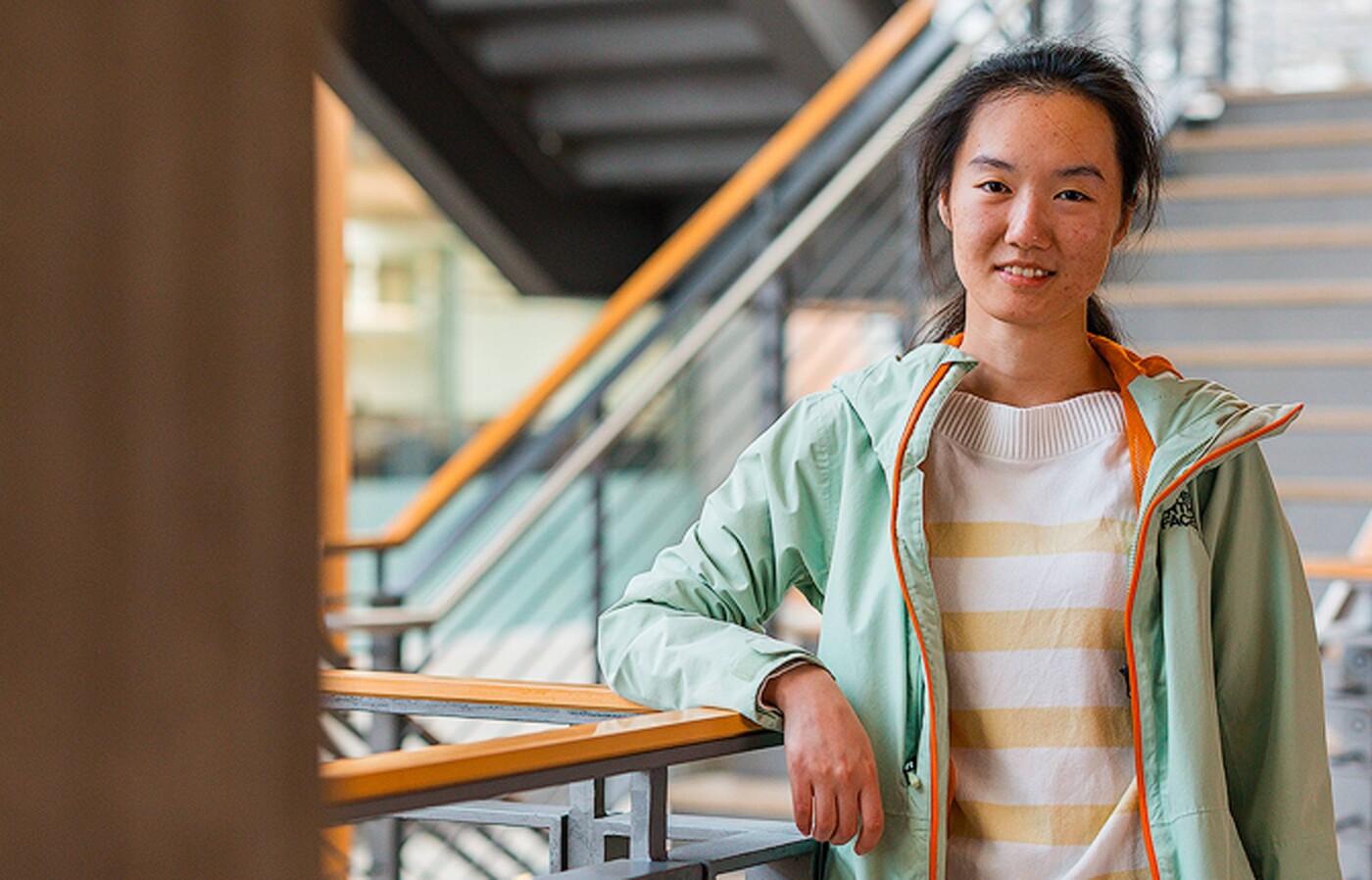 Xuan Wu leans against a railing, smiling at the camera inside Kelley Engineering.