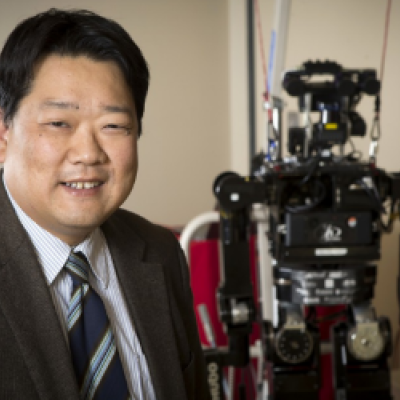 A researcher wearing a suit. On his right is a robot standing.