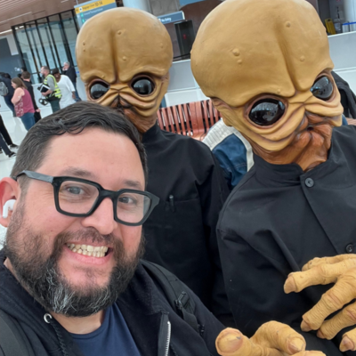 Man posing with two people in alien costumes.