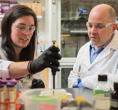 Two people wearing lab attire while working together in a lab.