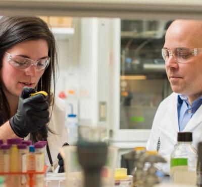 Two researchers wearing lab attire while working on a experiment.