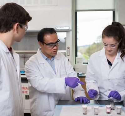 Professor guiding two students in lab uniform