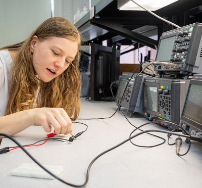 A student sitting at a workstation adjusting electrical testing and measurement equipment.