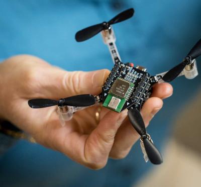 A hand holding a small drone with four propellers.