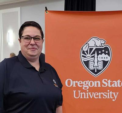 A person standing in front of an Oregon State University College of Engineering banner at an indoor event with others talking in the background.