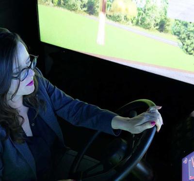 A person sitting in an indoor driving simulator with hands on the steering wheel.