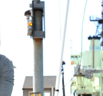 A person sitting outside looking at the camera with marine research equipment in the background.