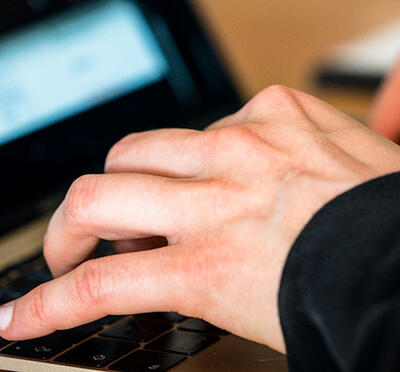 A person typing on a keyboard with a blurred digital screen in the background.