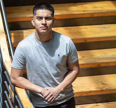A person stands on wooden stairs within a large atrium and looks up at the camera.