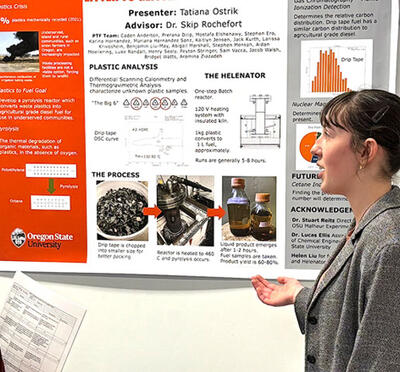 A woman presents a poster to a fellow student during a tabling event.