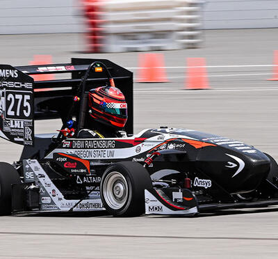 A race car with Oregon State University and corporate logos races around safety cones on a track.