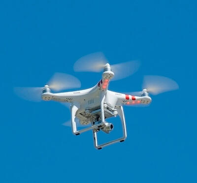 A drone hovers in the air against a clear blue sky.