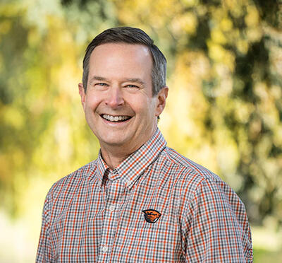 Smiling man wearing checkered shirted emblazoned with the Oregon State University beaver logo.
