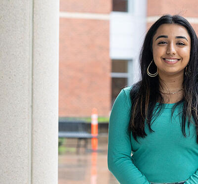 A person stands outside near a building column and smiles toward the camera.
