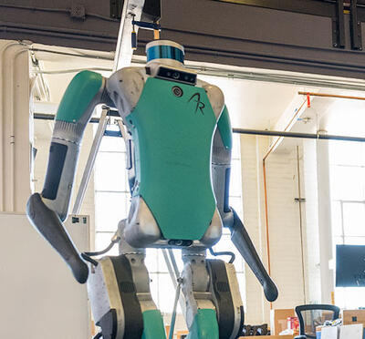A robot stands in a large indoor industrial setting. 