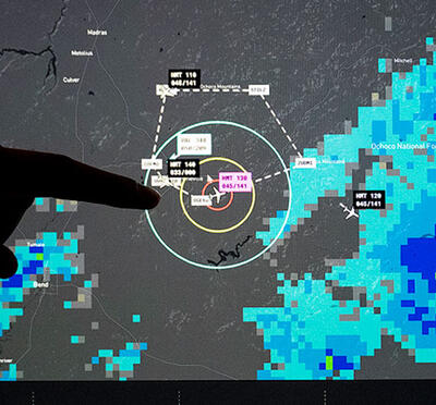 A person points to a monitor displaying air traffic control satellite imagery