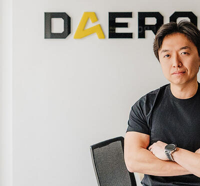 Alex Park posing with arms crossed in front of the DAERO company logo.