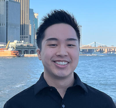 Chris Ho stands on a boat with the New York City skyline behind him.