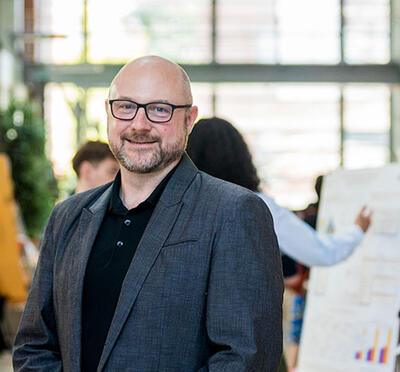 David Zier poses in Kelley Engineering Center atrium with presenters and posters in the background.