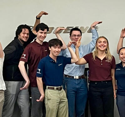 MECOP students in a conference room with the Boeing logo on the wall behind them and form the letters OSU with their arms.