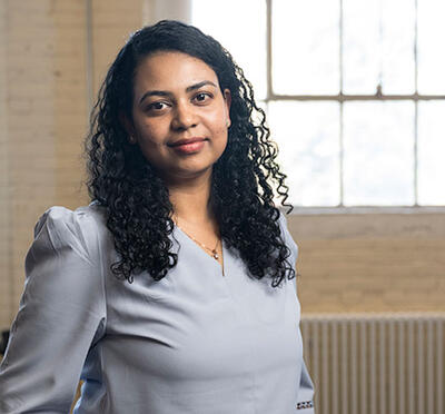 Sandhya Saisubramanian stands in a lab with windows behind her and workbenches and hardware in the background. 