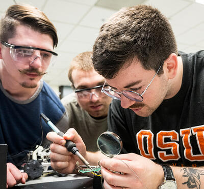 Three students soldering a circuit board. 