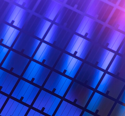 A close-up view of a semiconductor wafer with a repeating grid pattern of microelectronic structures in iridescent colors.
