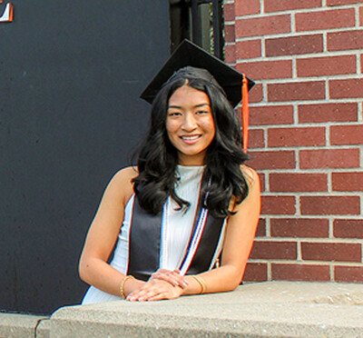 Megan Thomas wearing gradation cap and stole standing next to sign that says Oregon State University.