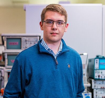 John Fletcher stands inside of a laboratory with testing equipment, workstations, and whiteboards in the background.