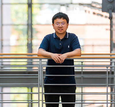 Xin Liang stands inside Kelley Engineering, a modern campus building with large windows in the background.