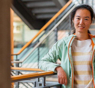 Xuan Wu leans against a railing, smiling at the camera inside Kelley Engineering.