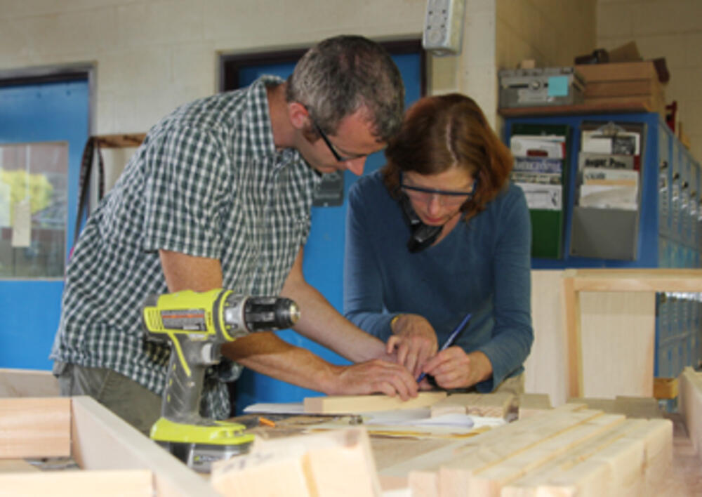 Two faculty members laying on a wooden table with a machine gun on their left.
