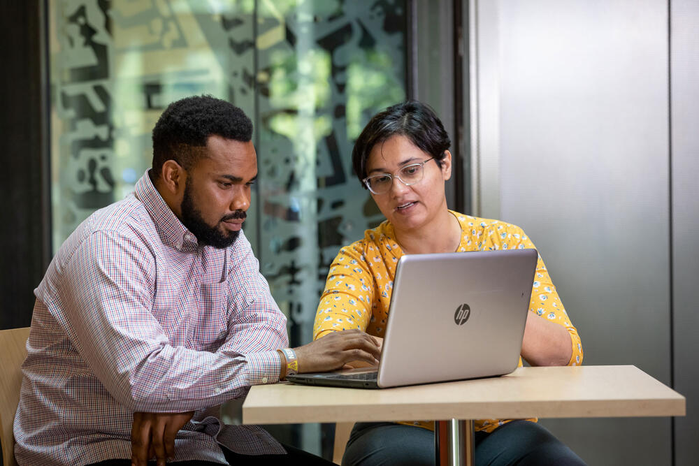 Meghna Babbar-Sebens and Justine Obiazi conversing while looking at a laptop.