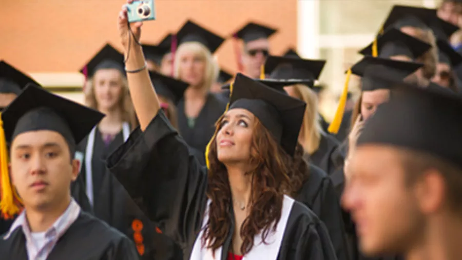 Student in graduate attire using their phone to record.