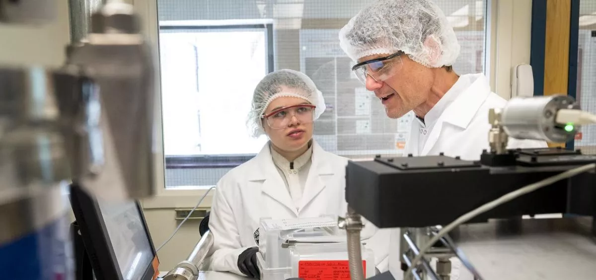 Two faculty members in lab uniform analyzing information