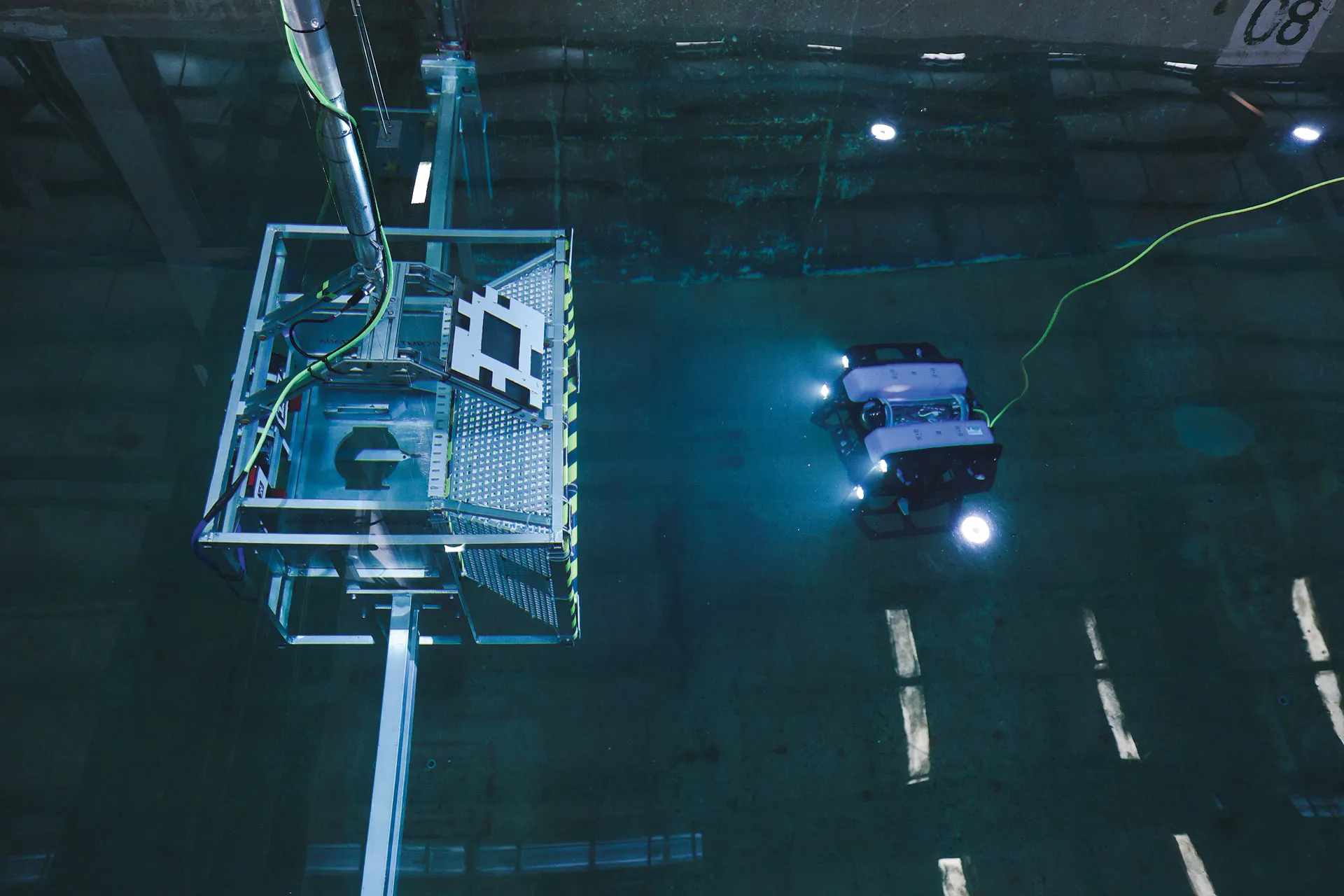 An underwater vehicle moving with a tether moving toward a docking station in a wave basin testing facility.