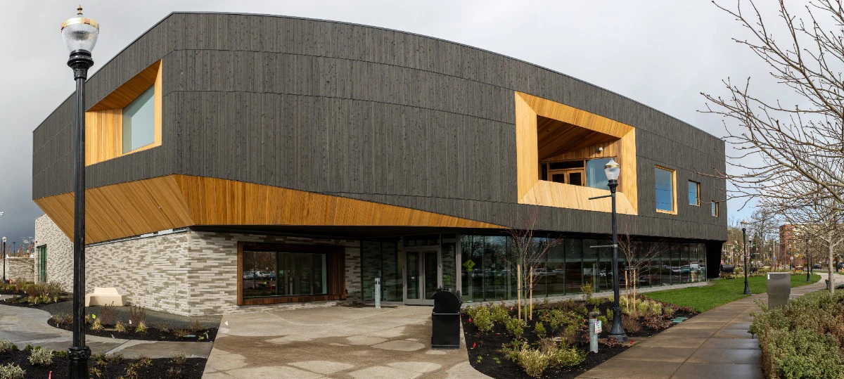The exterior of a performing arts facility with two large glass doors and sun shining on roof and walls.