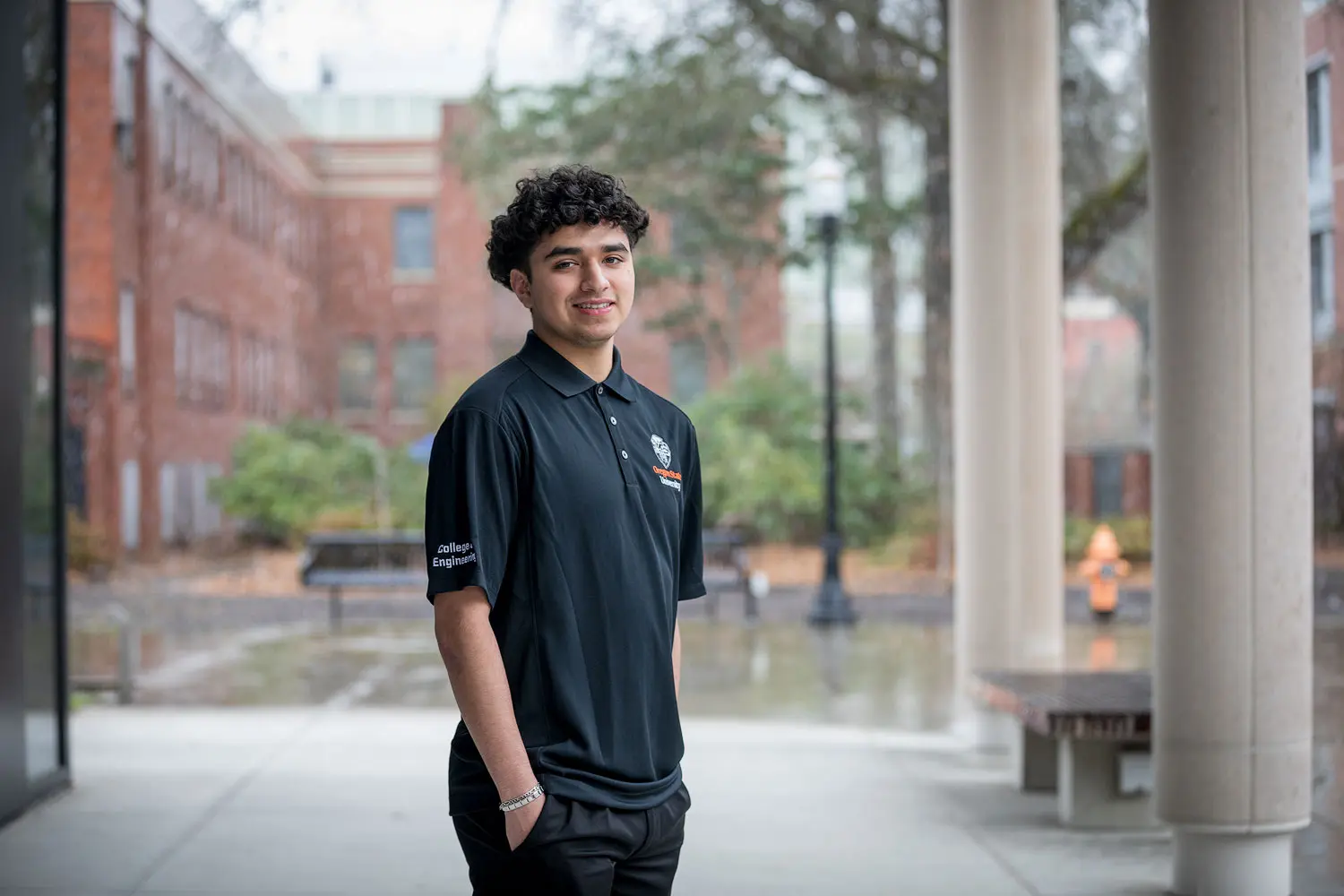 A person in an Oregon State University polo shirt stands near columns on campus and faces the camera smiling.