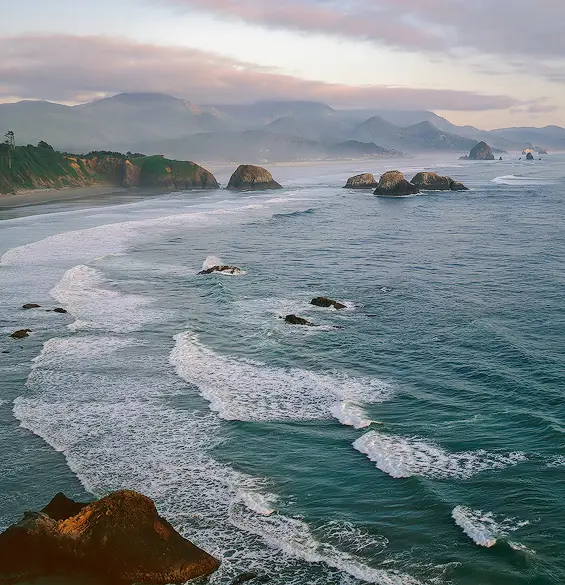 Pacific Northwest coastal view with mountains and ocean waves.