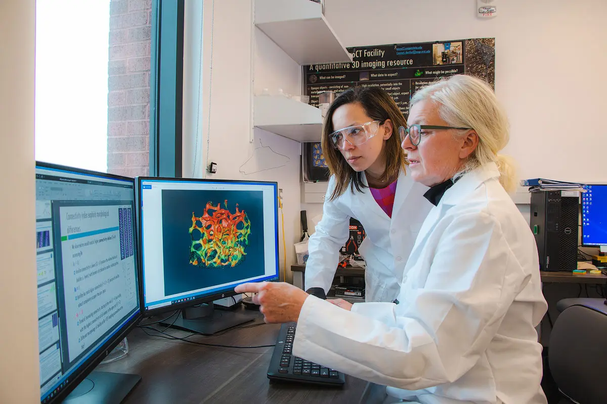 Two people in lab coats examine digital images on a screen.