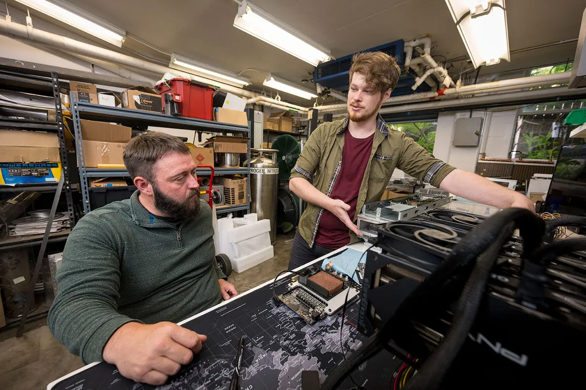 Two people in a lab look at hardware on workbench.